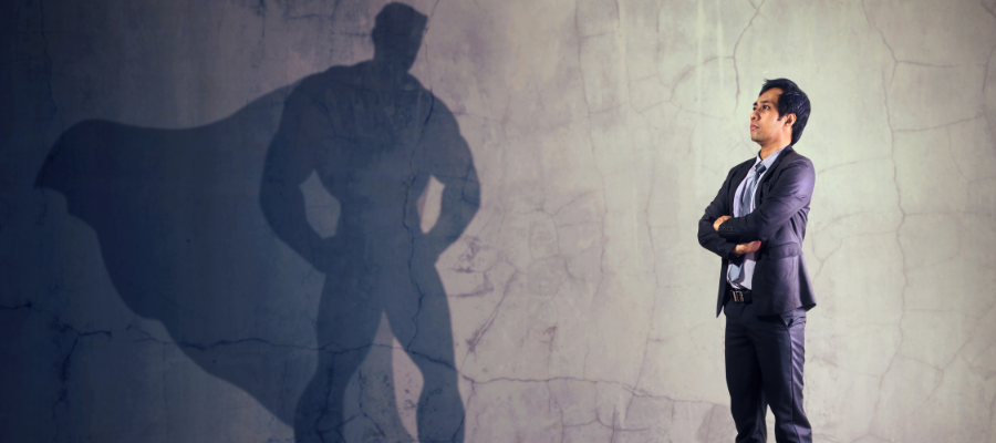 Businessman standing next to wall with shadow of superhero with cape.